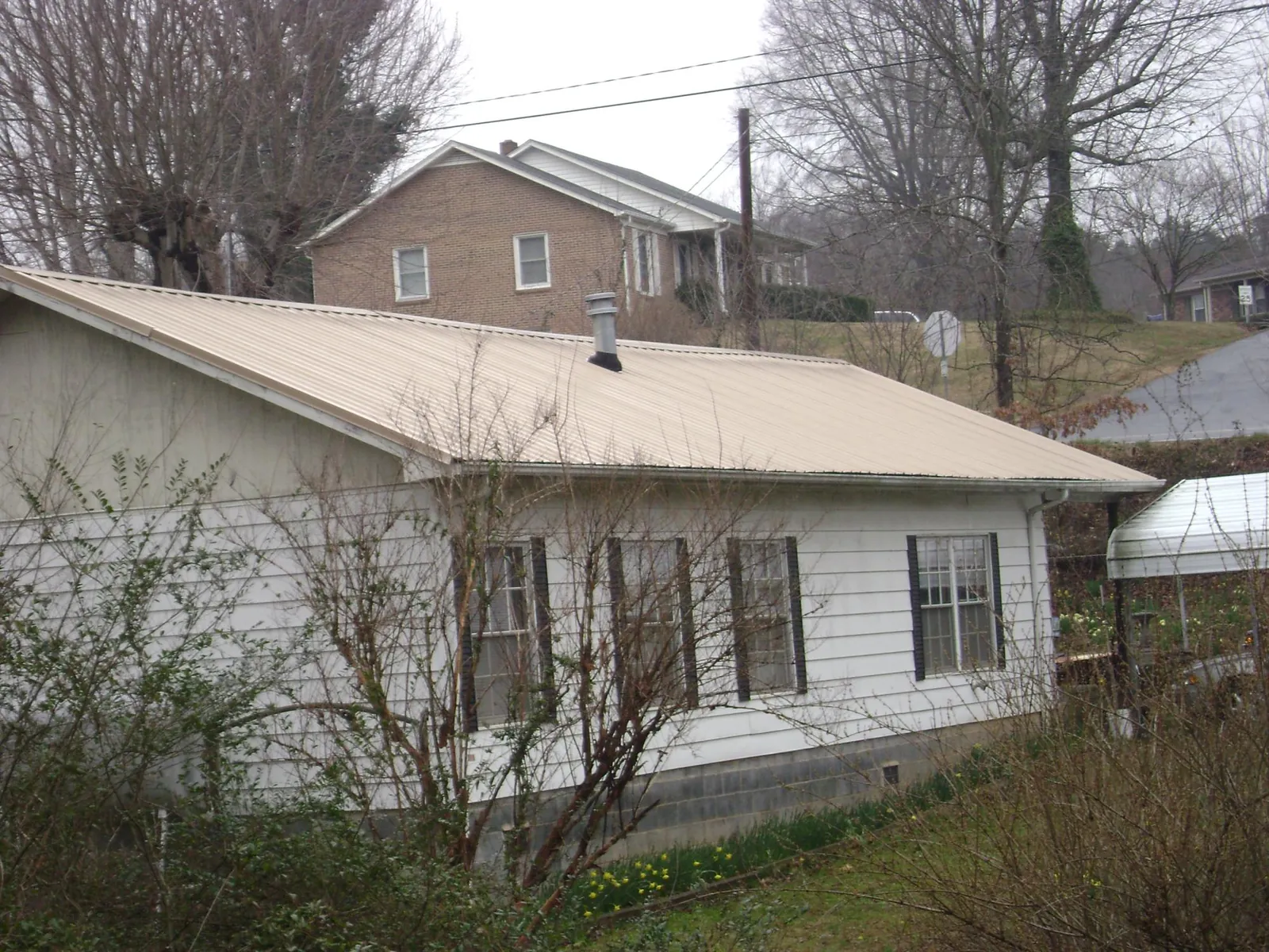 Tan metal roof on a white sided house set into a hillside — Commercial Roofing by Roofing Brothers in Hannibal
